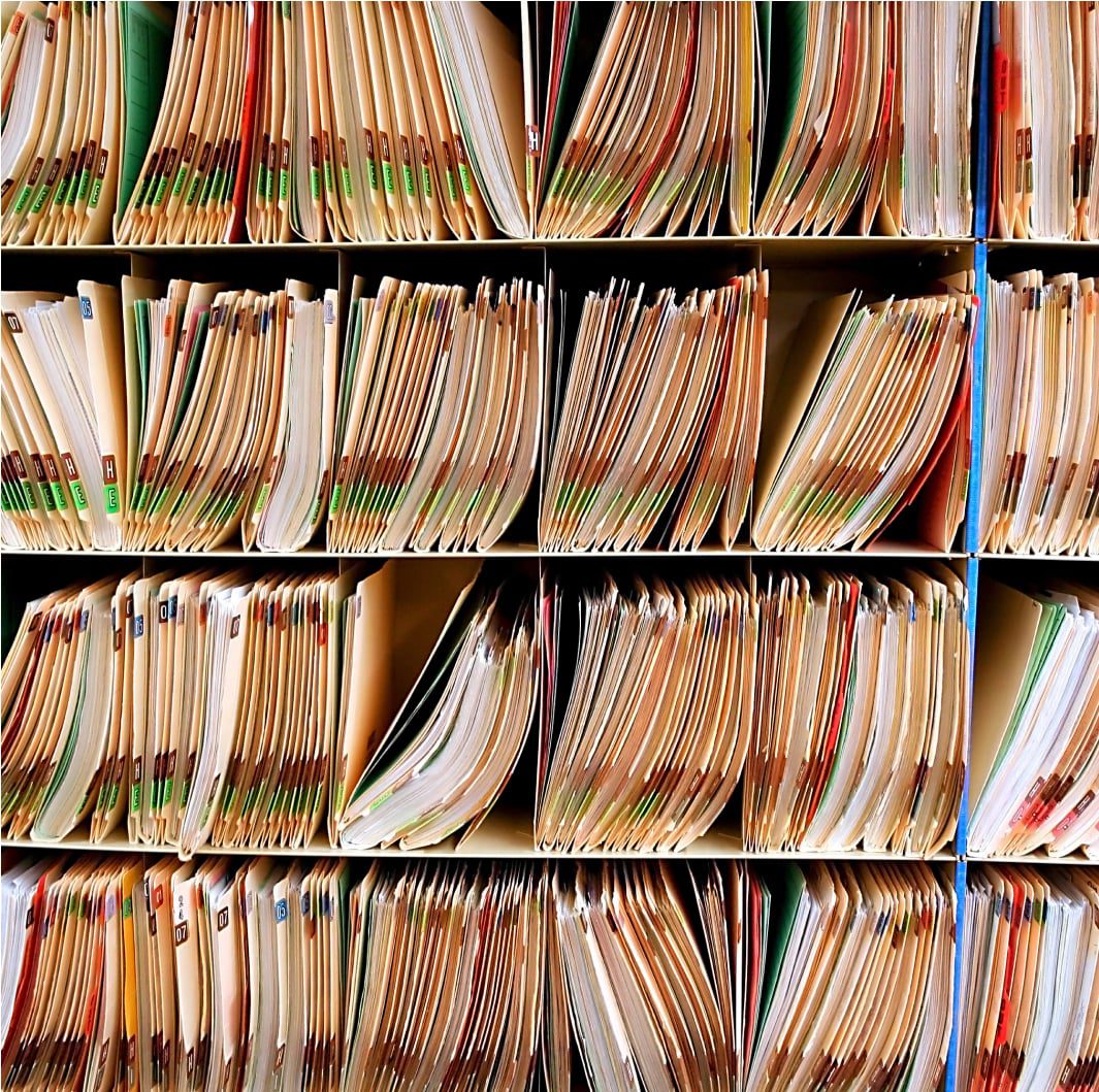 A neatly organized filing system consisting of several rows and columns of shelves filled with numerous labeled paper folders. Each folder is slightly open, revealing some documents inside, with tabs in various colors indicating different categories.